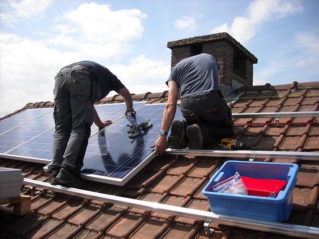 deux personne installe un panneau solaire sur un toit en tuiles mécanique page Aides
