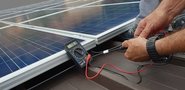 image montant un technicien faisant une mesure électrique avec un multimètre sur un panneau solaire
